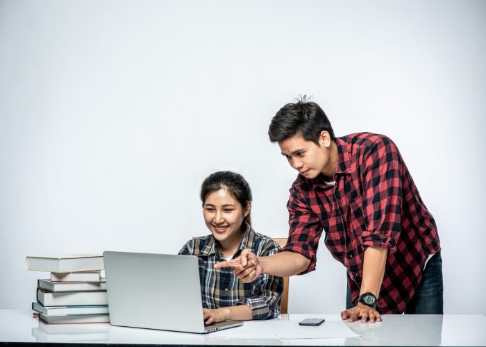 Men teach women how to work with laptops at work.